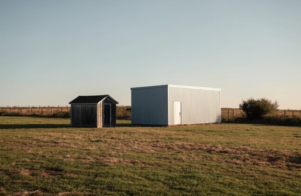 A small shed and a larger building side by side in a field for scale